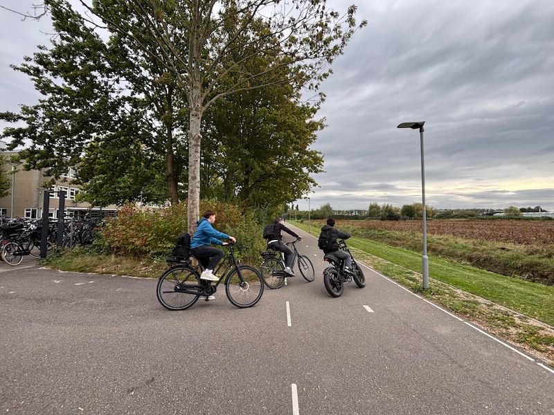 De fietsingang van het Cambium College (links), het fietspad en rechts het bruin gekleurde, bespoten veld.
